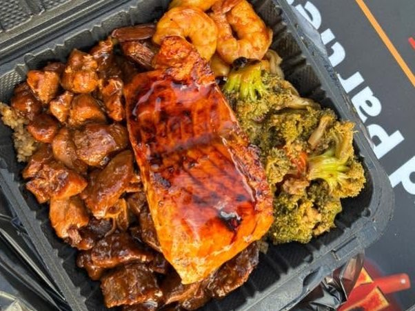 Glazed salmon fillet on steak bites with shrimp and broccoli in a takeout box