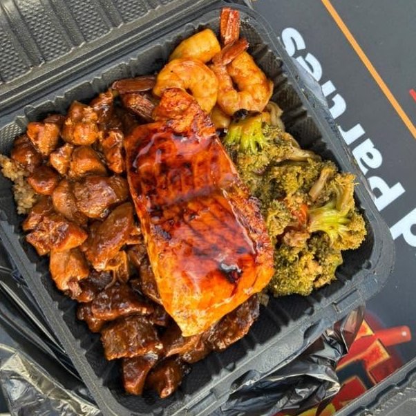Glazed salmon fillet on steak bites with shrimp and broccoli in a takeout box
