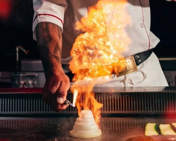 A hibachi chef sending a column of flame up from the griddle